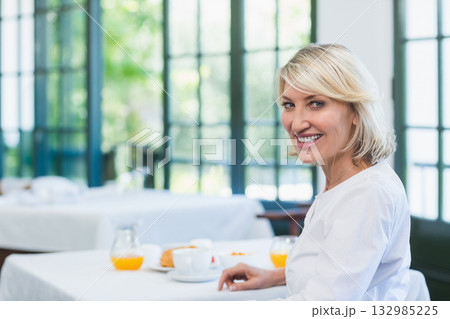 Middle-aged woman sitting at cafe at breakfast with coffee, pastry and orange juice, copy space Middle-aged woman sitting at cafe at breakfast with coffee, pastry and orange juice, copy space 132985225