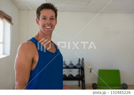 Smiling man in blue athletic top, dark shorts standing beside kettlebells rack in gym, copy space Smiling man in blue athletic top, dark shorts standing beside kettlebells rack in gym, copy space 132985226