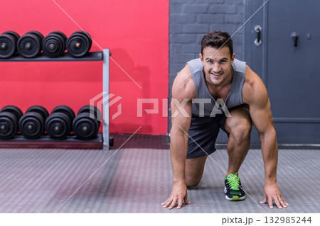 Male athlete getting into starting stance in gym with dumbbell rack and rubber floor, copy space 132985244