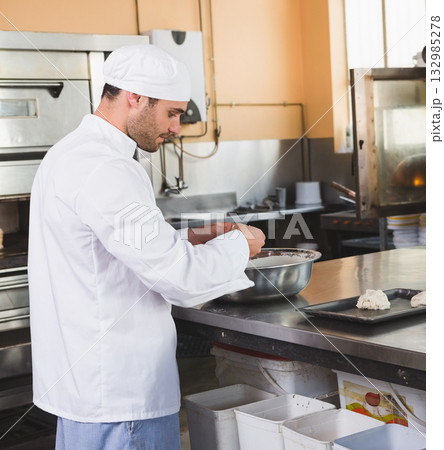Male chef in his 30s wearing chef coat shaping dough in commercial kitchen with mixing bowl Male chef in his 30s wearing chef coat shaping dough in commercial kitchen with mixing bowl 132985278