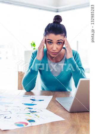 Woman working on laptop at wooden desk in bright office space, reviewing colorful charts Woman working on laptop at wooden desk in bright office space, reviewing colorful charts 132985283