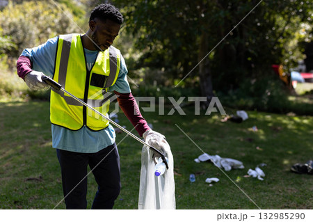 African American man picking up litter in park with metal picker and plastic-lined bag, copy space African American man picking up litter in park with metal picker and plastic-lined bag, copy space 132985290