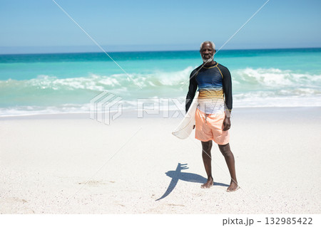 African American senior man standing on beach wearing swim shirt holding surfboard, copy space African American senior man standing on beach wearing swim shirt holding surfboard, copy space 132985422
