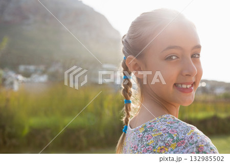 Child girl smiling in grassy field with blue braided hair ties and floral shirt, copy space 132985502