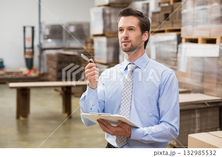 Man in his thirties standing by pallet table inspecting goods on clipboard in warehouse, copy space Man in his thirties standing by pallet table inspecting goods on clipboard in warehouse, copy space 132985532