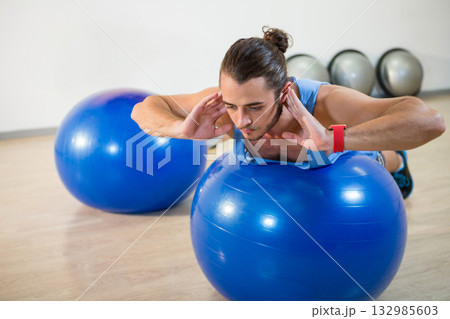Man in his twenties balancing on blue exercise ball with metallic gym balls at fitness studio 132985603