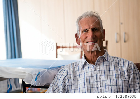 Senior man sitting beside hospital bed rails in patient room, smiling at camera, copy space Senior man sitting beside hospital bed rails in patient room, smiling at camera, copy space 132985639