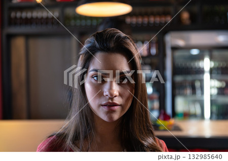 Woman in her twenties standing at bar counter in cafe under warm lamp with glass-front refrigerator Woman in her twenties standing at bar counter in cafe under warm lamp with glass-front refrigerator 132985640