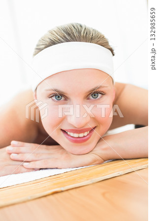 Female client lying on white towel covering wooden frame massage table in spa room wearing headband Female client lying on white towel covering wooden frame massage table in spa room wearing headband 132985659