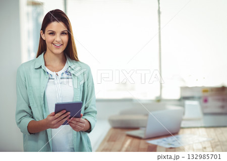Adult woman standing in studio holding tablet overlooking desk with laptop and printer and papers Adult woman standing in studio holding tablet overlooking desk with laptop and printer and papers 132985701