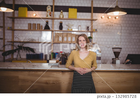 Woman barista wearing mustard blouse and apron operating espresso machine and POS terminal at café 132985728