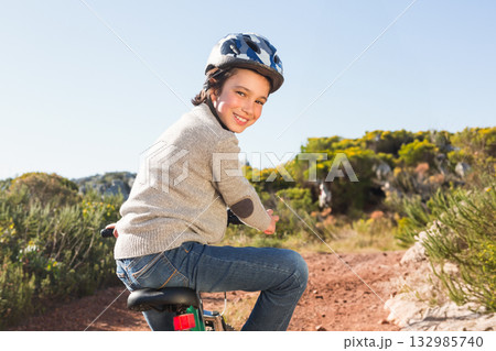 Boy wearing patterned helmet and sweater riding bicycle along dusty trail in scrub under blue sky Boy wearing patterned helmet and sweater riding bicycle along dusty trail in scrub under blue sky 132985740