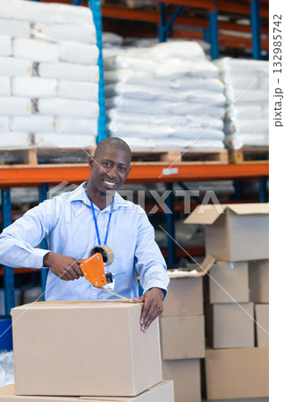 African American man in light blue shirt sealing box with tape dispenser at warehouse shelving African American man in light blue shirt sealing box with tape dispenser at warehouse shelving 132985742