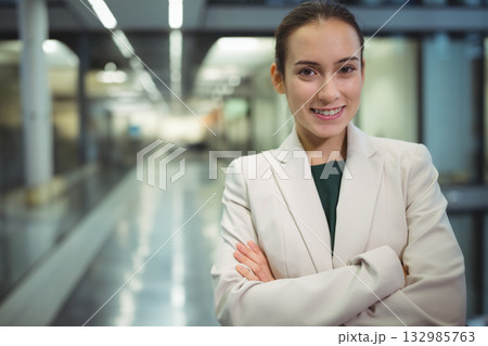 Professional woman folding arms facing camera in corporate corridor with glass walls, copy space 132985763