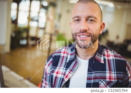 Mid adult man smiling while typing on keyboard near desk in open-plan office, copy space 132985764