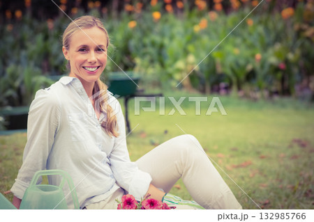 Woman gardener sitting on lawn tending pink flowers with watering can and wheelbarrow, copy space Woman gardener sitting on lawn tending pink flowers with watering can and wheelbarrow, copy space 132985766