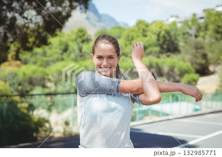 Woman stretching arm across chest on outdoor sports court with fence railing and court lines Woman stretching arm across chest on outdoor sports court with fence railing and court lines 132985771