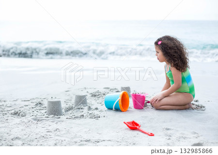 Female child kneeling molding sand towers at beach with colorful buckets and red spade, copy space 132985866