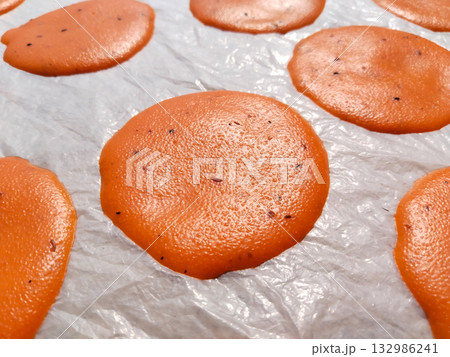 Spoon spreading small circular suji papad portions on plastic sheet for sun drying, traditional Indian snack preparation method in rural setting 132986241