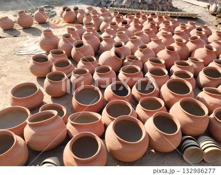 Multiple traditional earthen pots (handi) arranged on the ground for drying under the sun, symbolizing rural craftsmanship and pottery culture in Indian villages. 132986277