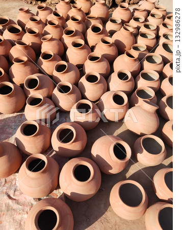 Freshly fired clay pots hand-painted with saffron color and sun-dried in open space for final setting, traditional Indian earthenware pottery placed for curing and long-term storage in sunlight. Freshly fired clay pots hand-painted with saffron color and sun-dried in open space for final setting, traditional Indian earthenware pottery placed for curing and long-term storage in sunlight. 132986278