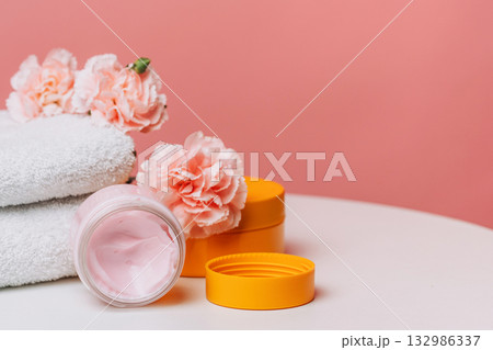 Pink moisturizer jar with carnations and towels 132986337