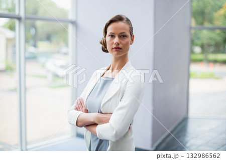 Woman in blazer standing crossing arms by pillar in office lobby facing parked car past windows8691 132986562