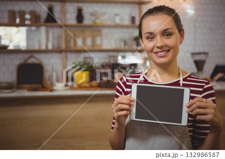 Female barista in gray apron holding tablet behind counter with pastries and jars, copy space Female barista in gray apron holding tablet behind counter with pastries and jars, copy space 132986587