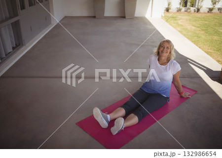 Senior woman stretching on pink exercise mat on porch wearing activewear and sneakers, copy space 132986654
