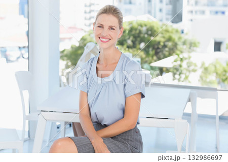 Smiling woman sitting at balcony table surrounded by white chairs, railing, and high-rise buildings Smiling woman sitting at balcony table surrounded by white chairs, railing, and high-rise buildings 132986697