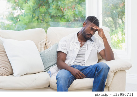 African American man sitting in living room on sofa with pillows rubbing forehead, copy space African American man sitting in living room on sofa with pillows rubbing forehead, copy space 132986711