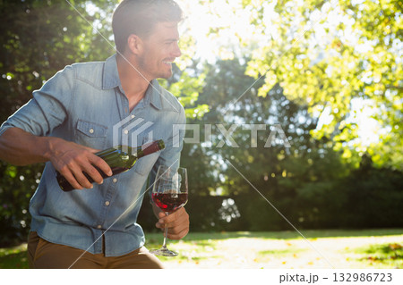 Man in denim shirt pouring red wine into glass on lawn under leafy trees, copy space Man in denim shirt pouring red wine into glass on lawn under leafy trees, copy space 132986723