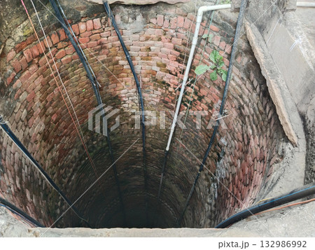 Brick-lined traditional well interior with multiple plastic pipes installed for submersible pump system in rural Indian irrigation setup 132986992