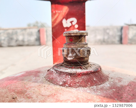 Close-up of red LPG gas cylinder valve nozzle head used in Indian households for cooking fuel, showing metal regulator area and safety design in detail 132987006