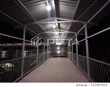 Railway station foot overbridge at night with roof and lights empty pedestrian walkway over train tracks 132987024