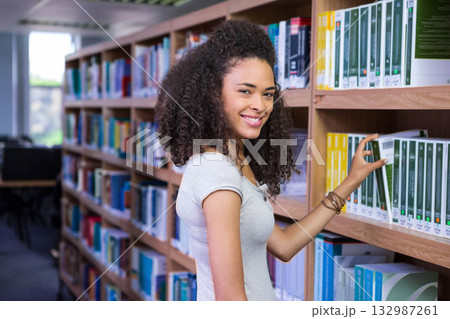 African American woman standing in library aisle pulling textbook from wooden shelf, copy space African American woman standing in library aisle pulling textbook from wooden shelf, copy space 132987261