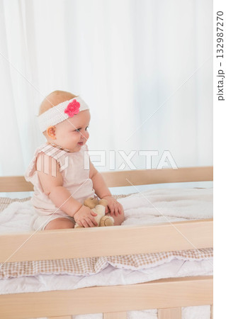 Child baby girl sitting on changing table in nursery wearing pink onesie holding plush teddy bear Child baby girl sitting on changing table in nursery wearing pink onesie holding plush teddy bear 132987270