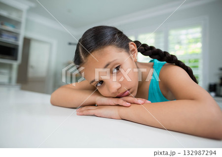 Girl leaning on white countertop by shuttered window in kitchen wearing turquoise top gazing out 132987294