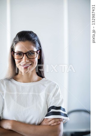Woman wearing rectangular glasses standing in office against wall with light strips, blurred chair Woman wearing rectangular glasses standing in office against wall with light strips, blurred chair 132987431