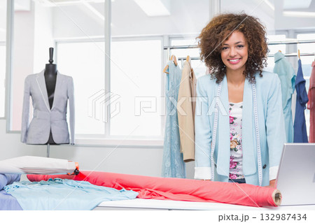 African American woman standing at cutting table in studio measuring fabric with tape near laptop African American woman standing at cutting table in studio measuring fabric with tape near laptop 132987434