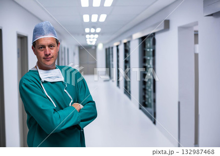 Male surgeon standing in hospital corridor wearing green scrubs, bouffant cap and mask, copy space Male surgeon standing in hospital corridor wearing green scrubs, bouffant cap and mask, copy space 132987468
