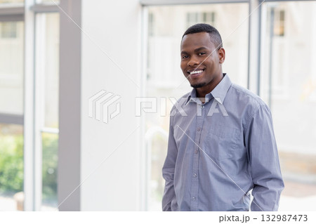 African American man standing in office lobby by large glass windows with green foliage, copy space African American man standing in office lobby by large glass windows with green foliage, copy space 132987473