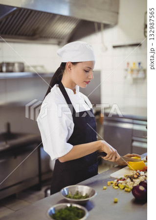 Native American female chef wearing chef coat chopping peppers eggplant herbs on board in kitchen Native American female chef wearing chef coat chopping peppers eggplant herbs on board in kitchen 132987565