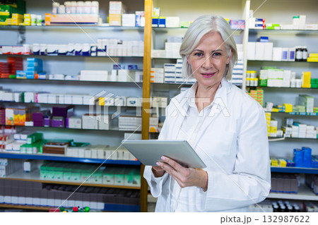 Senior female pharmacist holding tablet organizing medication on pharmacy shelves, copy space Senior female pharmacist holding tablet organizing medication on pharmacy shelves, copy space 132987622