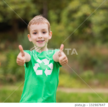 Boy smiling at camera and giving thumbs up in grassy park wearing green recycling t-shirt Boy smiling at camera and giving thumbs up in grassy park wearing green recycling t-shirt 132987647