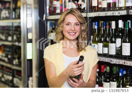 Woman holding green wine bottle and smiling in liquor store aisle with metal shelving Woman holding green wine bottle and smiling in liquor store aisle with metal shelving 132987653