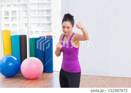 Asian woman practicing boxing stance on floor in fitness studio with foam rollers, exercise balls 132987672