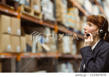 Woman standing in warehouse aisle wearing headset and blazer checking cardboard boxes, copy space Woman standing in warehouse aisle wearing headset and blazer checking cardboard boxes, copy space 132987676