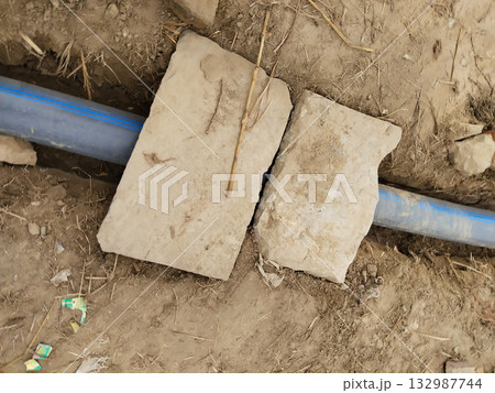 Rural irrigation pipeline covered with planks on mud road near farmland, allowing pedestrian movement while enabling discreet water supply setup in Indian village outskirts 132987744