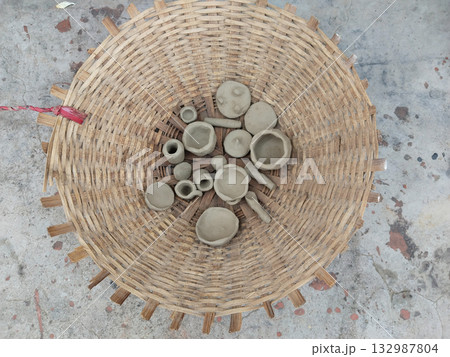 Child-made miniature clay utensils in a bamboo basket depicting traditional Indian folk art, rural childhood, and handcrafted cultural expressions in earthy tones and textures 132987804